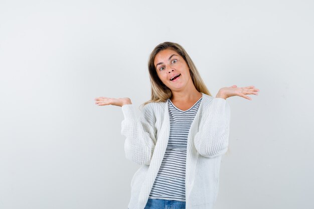 Mujer joven haciendo gesto de bienvenida en camiseta, chaqueta y mirando alegre, vista frontal.