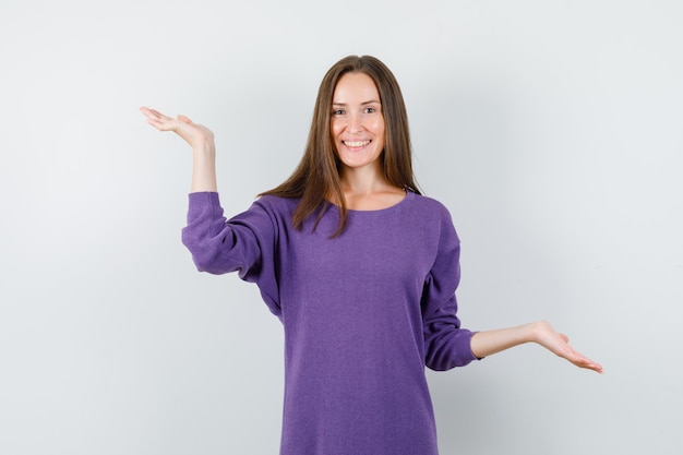 Mujer joven haciendo gesto de escalas en camisa violeta y mirando feliz. vista frontal.