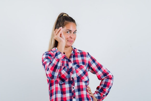 Mujer joven haciendo gesto italiano en camisa casual y mirando feliz. vista frontal.