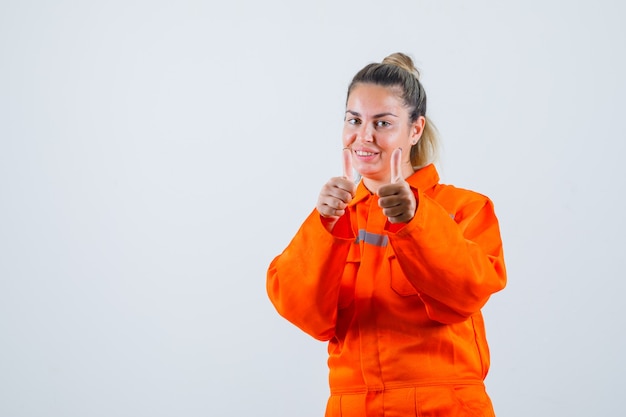 Mujer joven haciendo un gesto positivo con las manos en uniforme de trabajador y mirando exitoso, vista frontal.