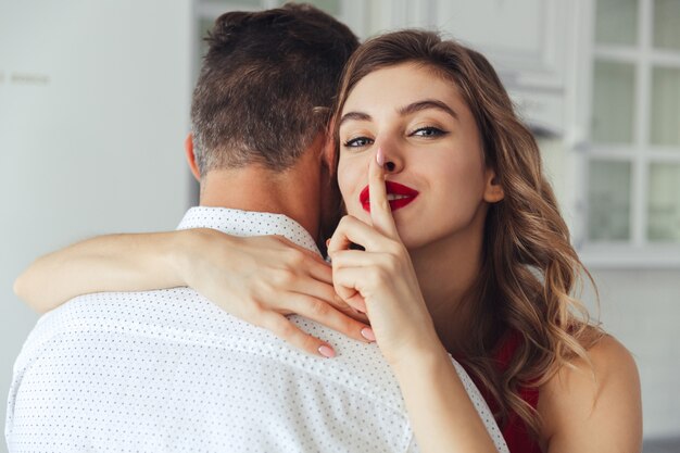 Mujer joven haciendo un gesto de silencio mientras abraza a su marido