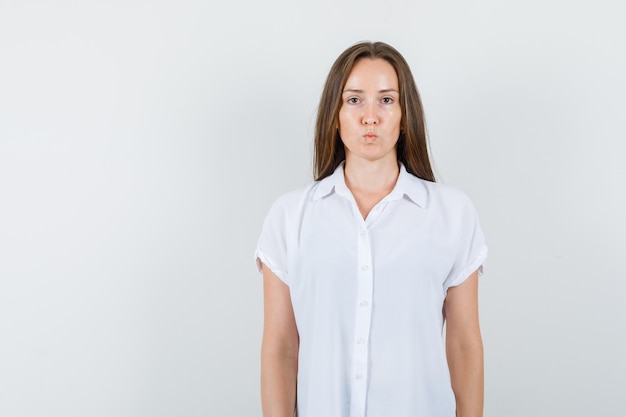 Foto gratuita mujer joven haciendo pucheros con los labios en una blusa blanca y luciendo raro