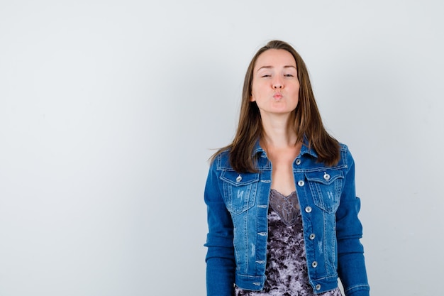 Mujer joven haciendo pucheros con los labios en la chaqueta de mezclilla y luciendo pacífica. vista frontal.