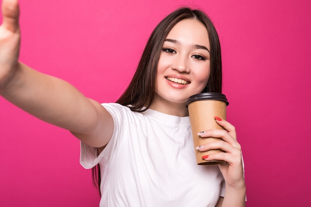 Mujer joven haciendo selfie con su taza de café en la pared de color rosa.