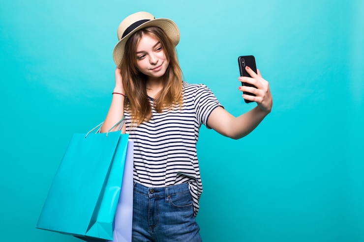 Foto gratuito mujer joven haciendo una selfie en su teléfono inteligente sentado con bolsas de colores para ir de compras