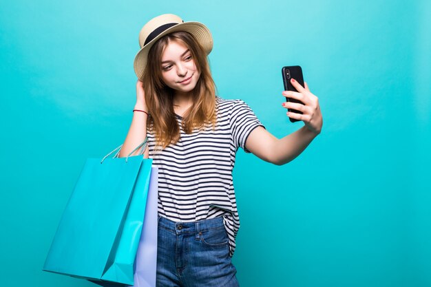 Mujer joven haciendo una selfie en su teléfono inteligente sentado con bolsas de colores para ir de compras