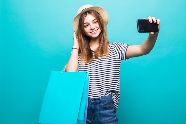 Mujer joven haciendo una selfie en su teléfono inteligente sentado con bolsas de colores para ir de compras