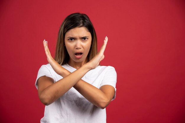 Mujer joven haciendo señal de stop con las manos en la pared roja.