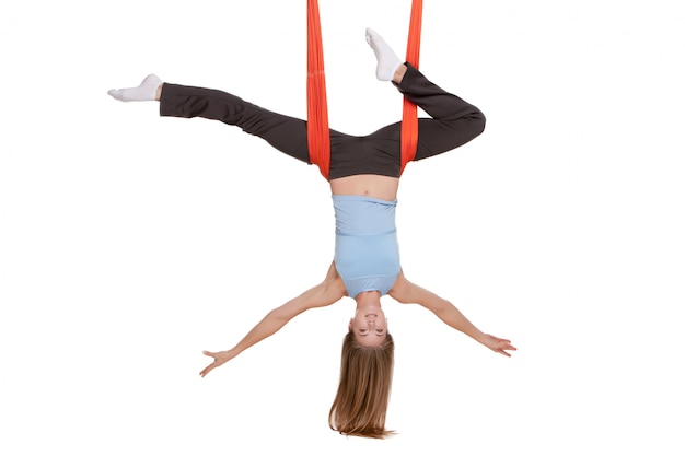 Mujer joven haciendo yoga aéreo antigravedad en hamaca en la pared blanca