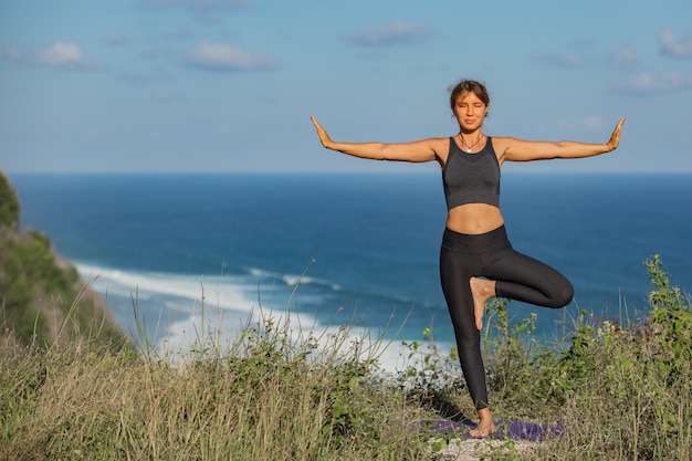 Mujer joven haciendo yoga al aire libre con una increíble vista posterior. Bali. Indonesia.