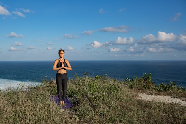 Mujer joven haciendo yoga al aire libre con una increíble vista posterior. Bali. Indonesia.
