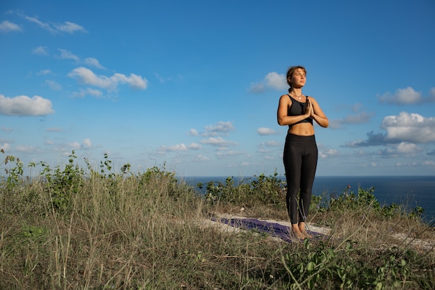 Mujer joven haciendo yoga al aire libre con una increíble vista posterior. Bali. Indonesia.