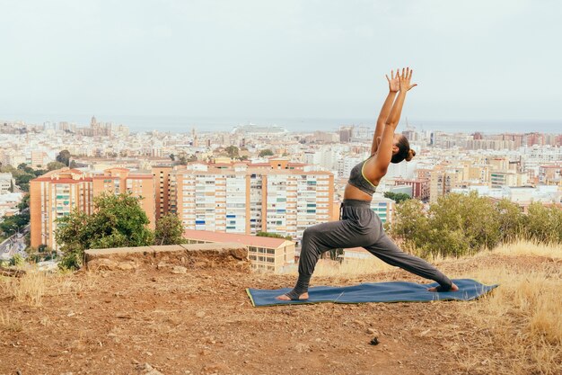 Mujer joven haciendo yoga y la ciudad detrás