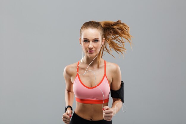 Mujer joven hermosa de los deportes que corre música que escucha aislada por los auriculares.