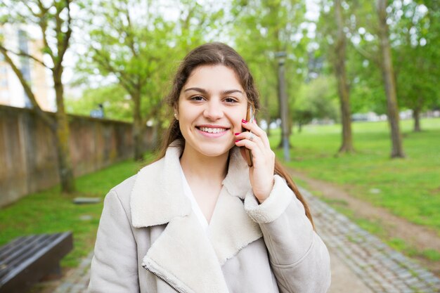 Mujer joven hermosa feliz que invita al teléfono en parque