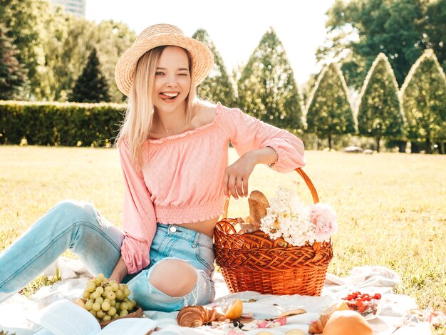 Mujer joven hermosa hipster en jeans de moda de verano, camiseta rosa y sombrero. Mujer despreocupada haciendo picnic afuera.