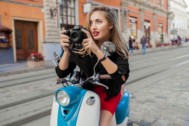 Foto gratuita mujer joven hermosa hipster montando con cámara de fotos en la calle de la ciudad de moto