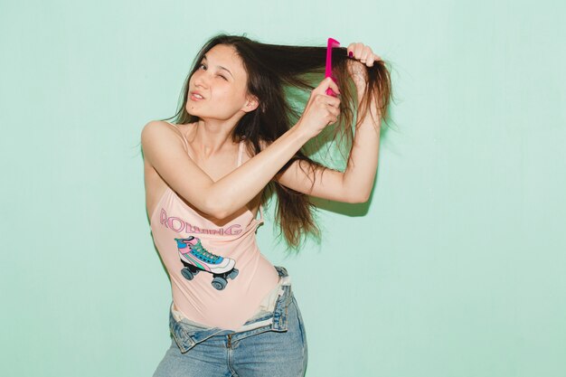 Mujer joven hermosa hipster posando contra la pared azul, peinando el pelo largo