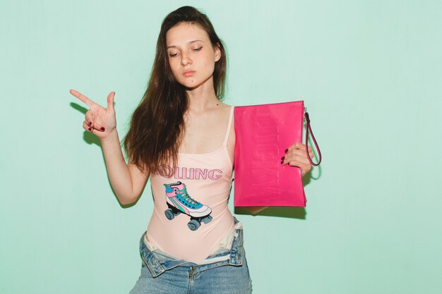 Mujer joven hermosa hipster posando contra la pared azul, sosteniendo el embrague de moda rosa en la mano