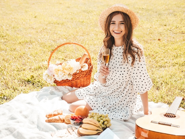 Mujer joven hermosa hipster en vestido de verano de moda y sombrero. Mujer despreocupada haciendo picnic afuera.