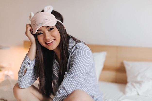 Mujer joven en hermosa máscara para dormir con sonrisa mira al frente