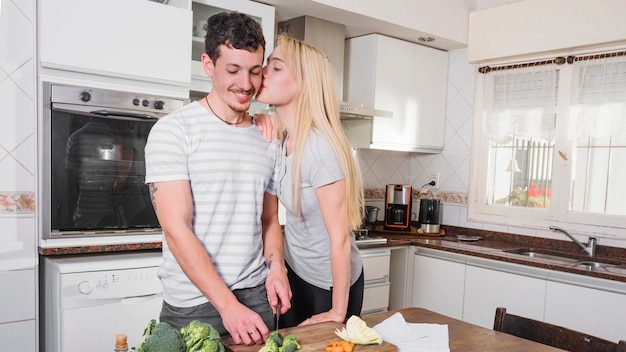 Mujer joven hermosa que ama a su marido que corta bróculi en la cocina