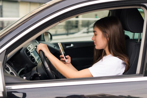 Mujer joven hermosa que escribe sms mientras conduce el coche.