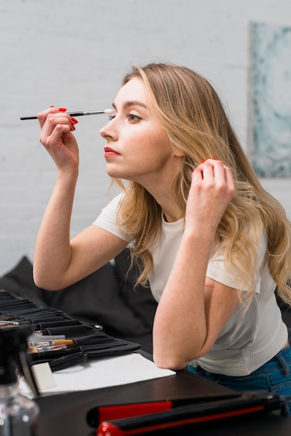 Mujer joven hermosa que se hace maquillaje que se sienta en estudio