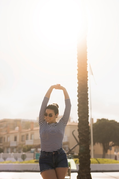 Mujer joven hermosa que lleva las gafas de sol que estiran sus manos en jardín