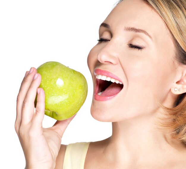 Mujer joven hermosa que muerde el morder una manzana madura fresca en blanco.