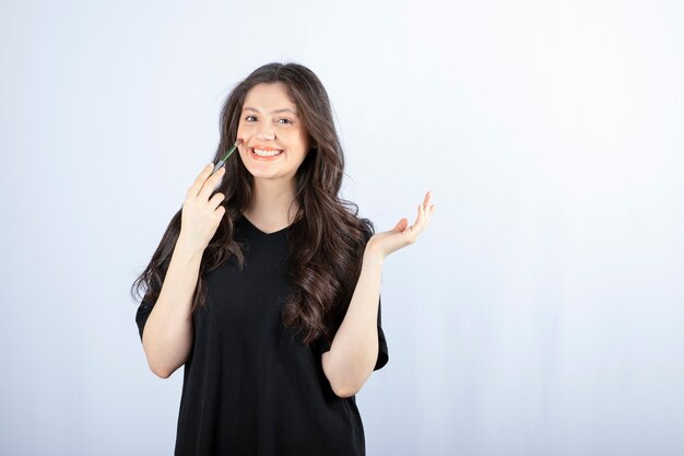 Mujer joven hermosa que pone rubor con el cepillo cosmético sobre la pared blanca.