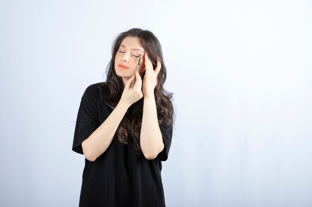 Mujer joven hermosa que pone sombra con el cepillo cosmético sobre la pared blanca.