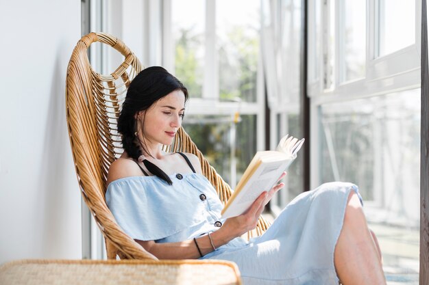 Mujer joven hermosa que se sienta en el libro de lectura de la silla