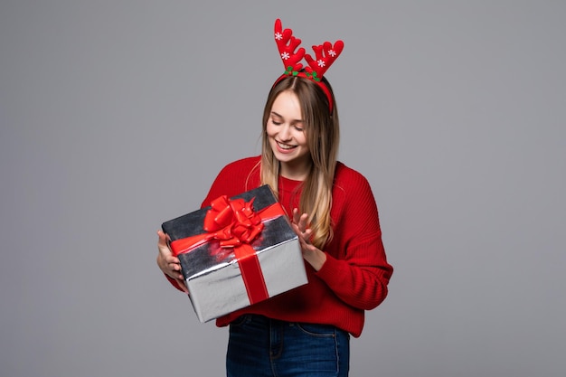 Mujer joven hermosa que sostiene el desgaste de la caja de regalo en cuernos rojos en la pared gris