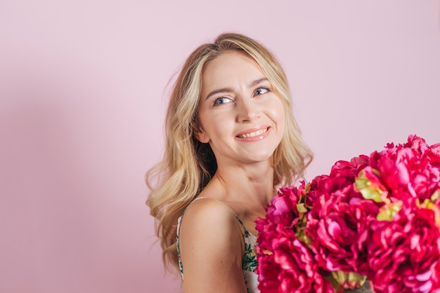 Mujer joven hermosa que sostiene el ramo color de rosa contra fondo rosado