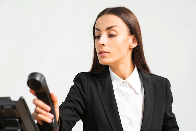 Foto gratuita mujer joven hermosa que sostiene el receptor de teléfono contra el fondo blanco