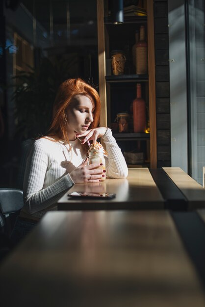 Mujer joven hermosa que sostiene el tarro del smoothie en el café