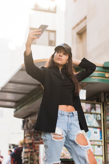 Foto gratuita mujer joven hermosa que toma el selfie en el teléfono móvil que se coloca en la calle