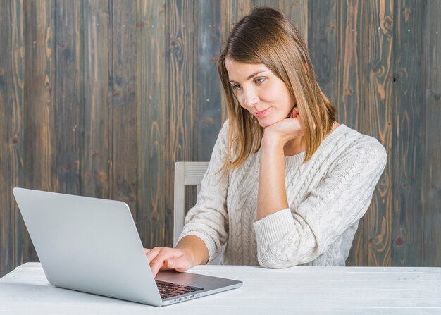 Mujer joven hermosa que trabaja en la computadora portátil sobre el escritorio