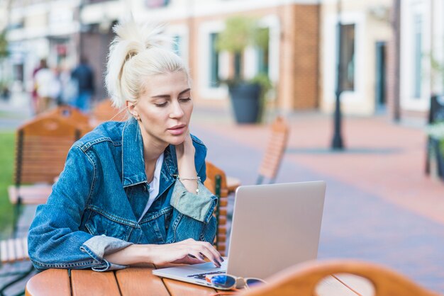 Mujer joven hermosa que usa la computadora portátil en al aire libre