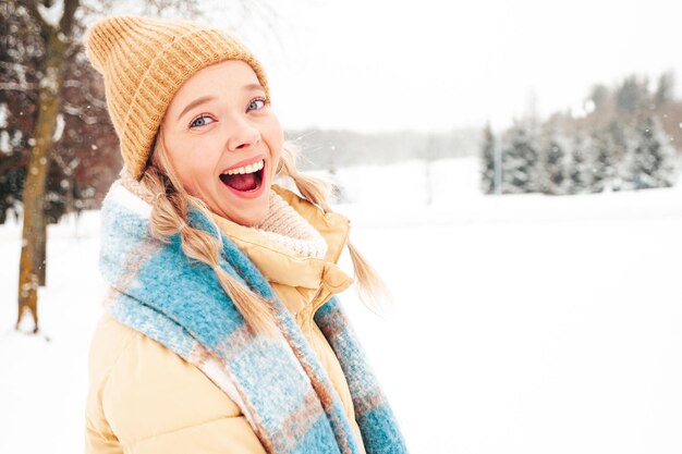 Mujer joven hermosa sonriente hipster en ropa de abrigo de moda y bufanda. Mujer despreocupada posando en la calle en el parque. Modelo puro positivo divirtiéndose en la nieve. Disfrutando de los momentos invernales