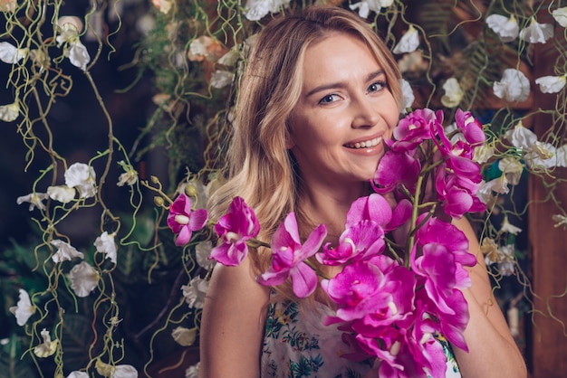 Mujer joven hermosa sonriente que lleva a cabo la rama de orquídeas rosadas