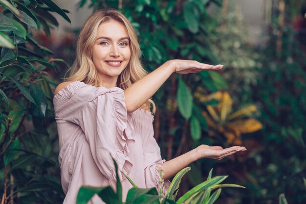 Mujer joven hermosa sonriente que muestra algo en las palmas de sus manos en el jardín