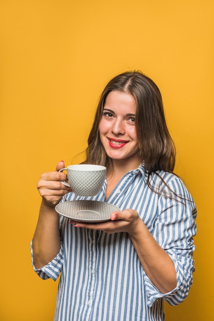 Mujer joven hermosa sonriente que sostiene la taza y el platillo en manos