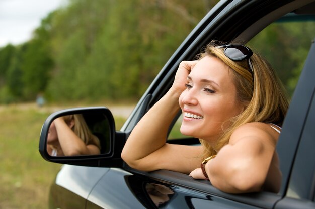 Mujer joven hermosa sonrisa en el coche nuevo - al aire libre