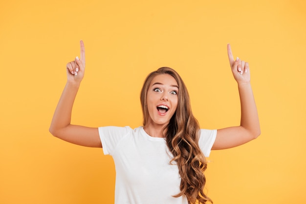 Mujer joven hermosa sorprendida emocionada que señala al copyspace.