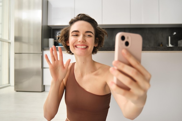 Foto gratuita mujer joven y hermosa usando el teléfono móvil y haciendo ejercicio en casa agitando la mano en los chats de video de teléfonos inteligentes d