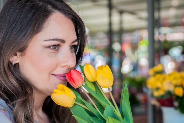 Mujer joven con hermoso ramo de tulipanes en el fondo de la tienda de flores. Retrato de una hembra bonita que sonríe mientras que sostiene los tulipanes frescos.