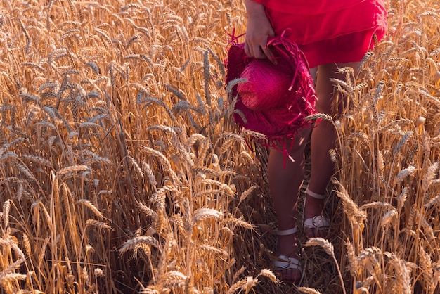 Mujer joven en un hermoso vestido rojo disfrutando del clima soleado en un campo de trigo
