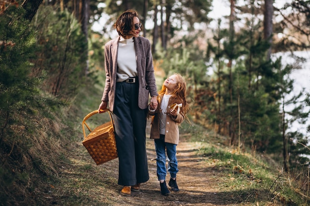 Mujer joven con hija en bosque con caja de picnic